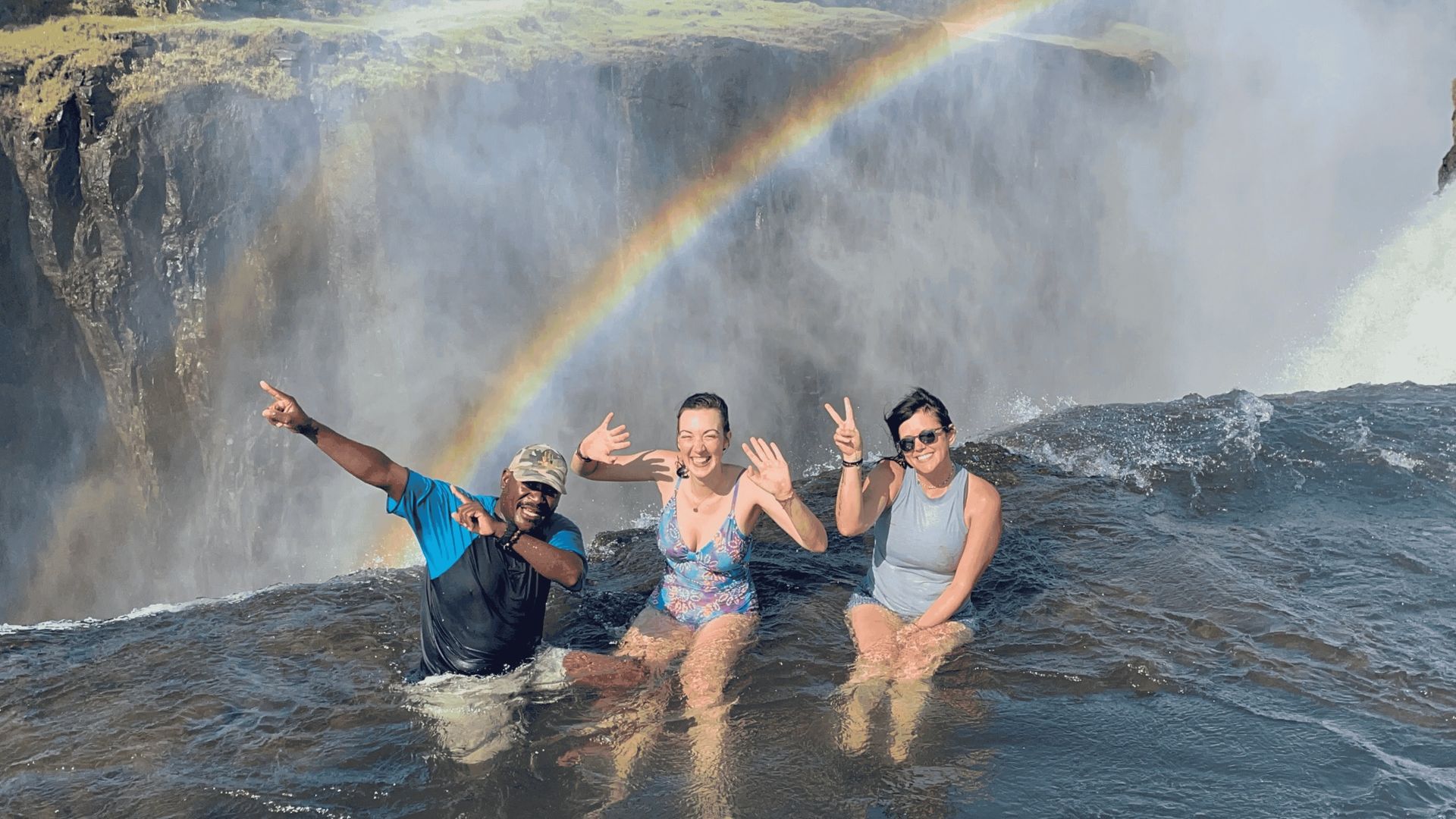 A group of people are standing in front of a waterfall with a rainbow in the background.