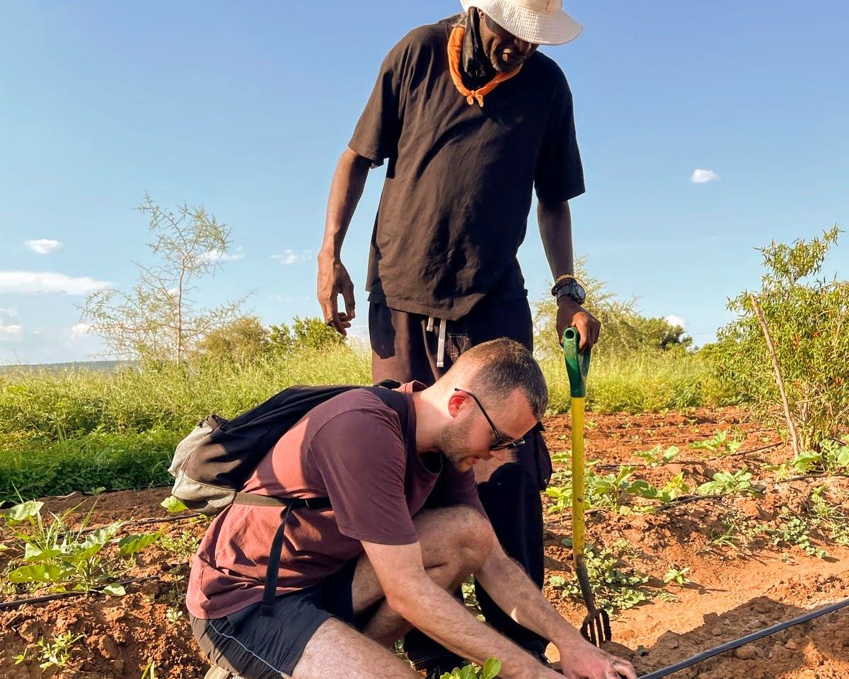 A man is kneeling down in a field while another man stands behind him.