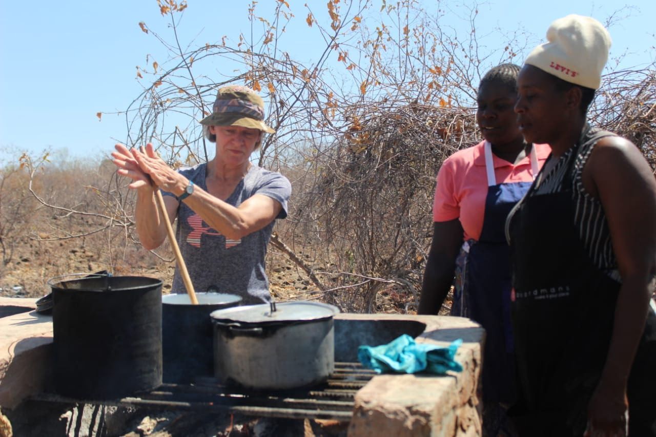 A group of women are standing around a stove with pots on it.