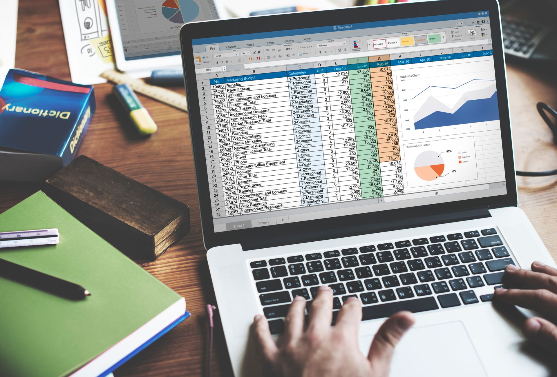 Laptop displaying spreadsheets and charts on a desk, with hands typing nearby