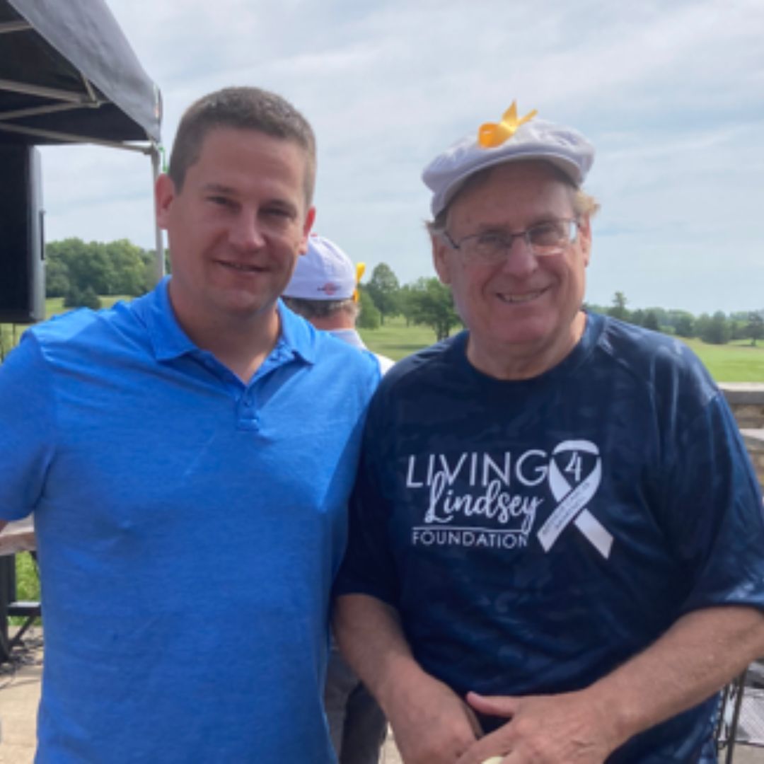 a man wearing a living4lindsey foundation shirt stands next to another man