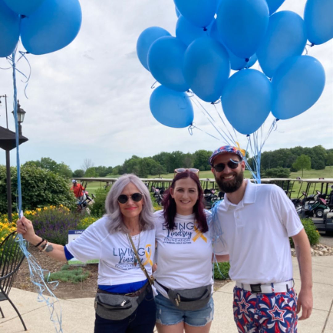 a woman wearing a living4lindsey shirt holds a bunch of blue balloons