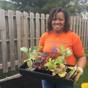 A woman in an orange shirt is holding a tray of plants.