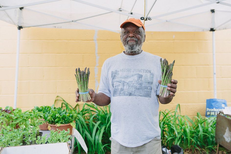 A man is holding two bunches of asparagus in front of a tent.