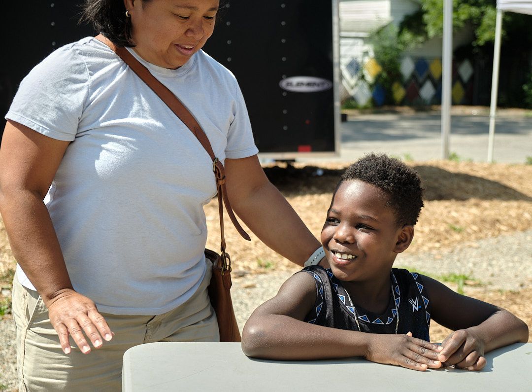 A woman is standing next to a young boy sitting at a table.