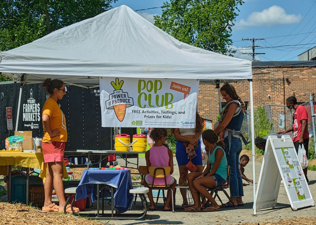 A group of children are sitting under a pop club tent.