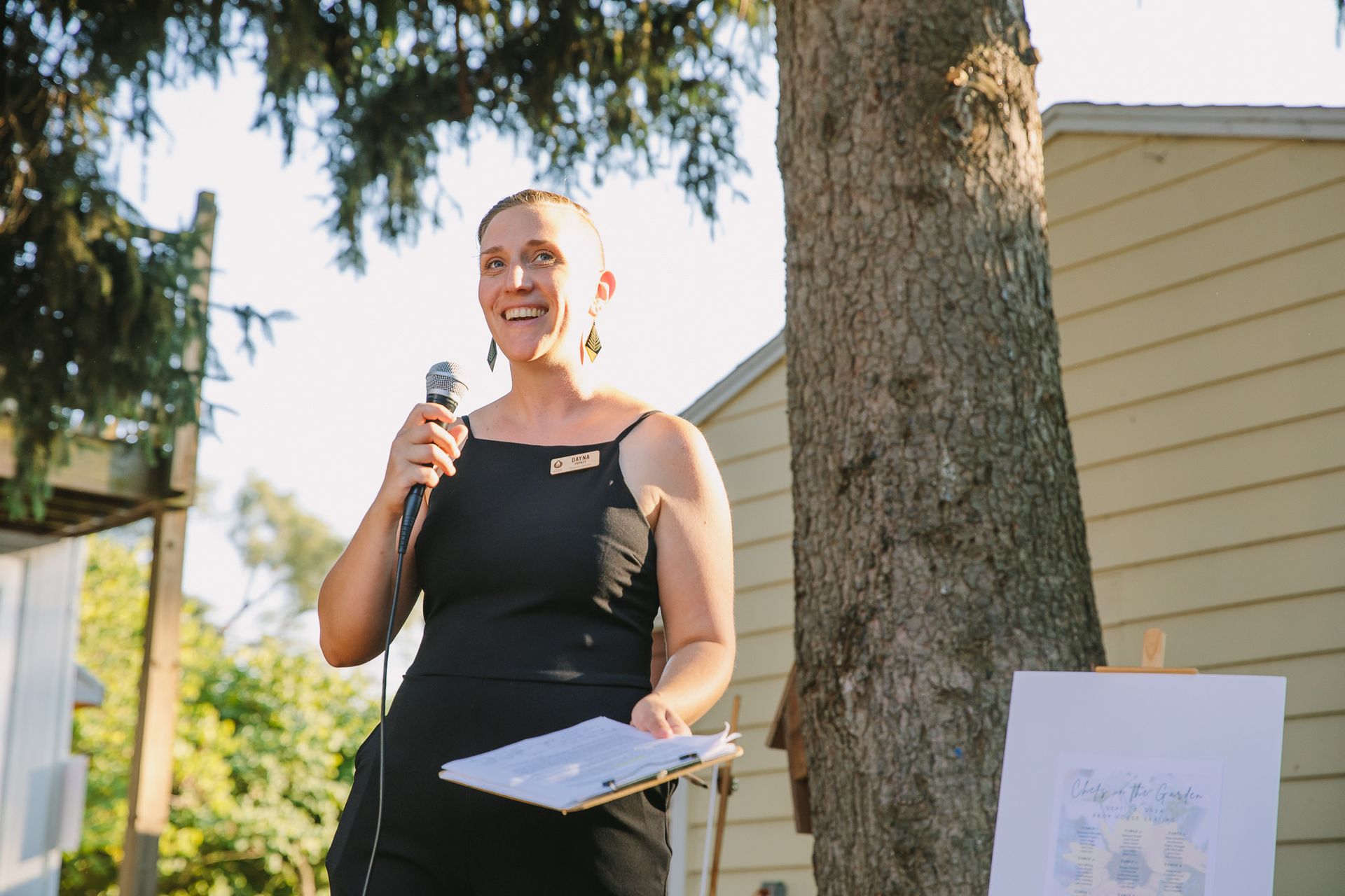 A woman in a black dress is holding a microphone and giving a speech.