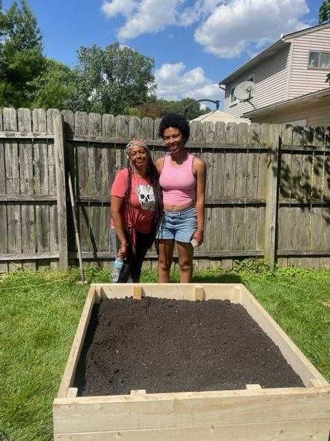 Two women are standing next to a wooden box in a backyard.