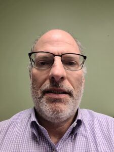 A man with a beard and glasses is wearing a purple shirt.