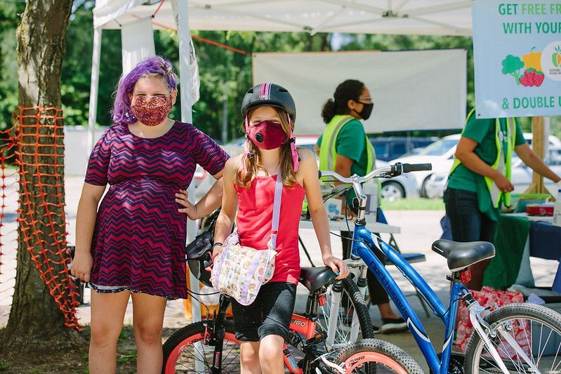 Two girls wearing face masks are standing next to bicycles.