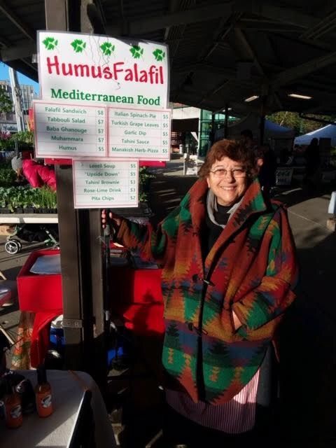 A woman stands in front of a humus falafel sign