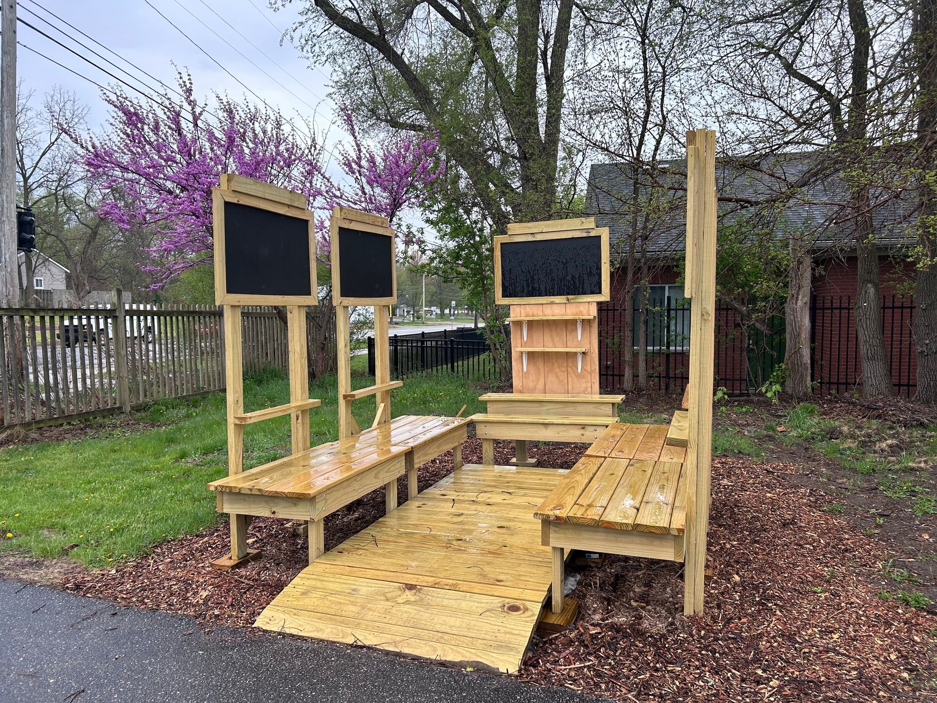 A wooden shelter with a ramp and chalkboards in a park.