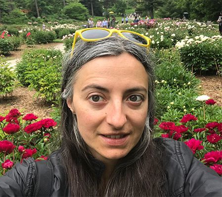 A woman wearing yellow sunglasses is taking a selfie in a garden.