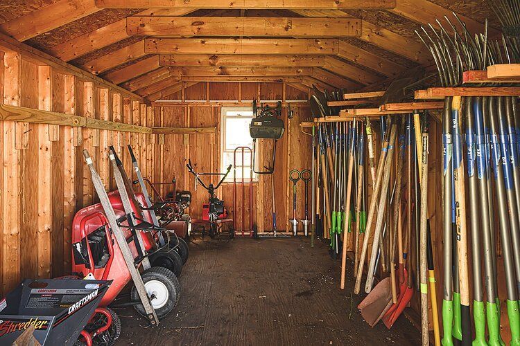 A wooden garage filled with lawn mowers and gardening tools.