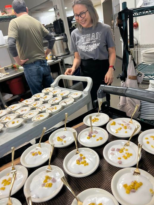 A woman is standing in a kitchen surrounded by plates of food and spoons.