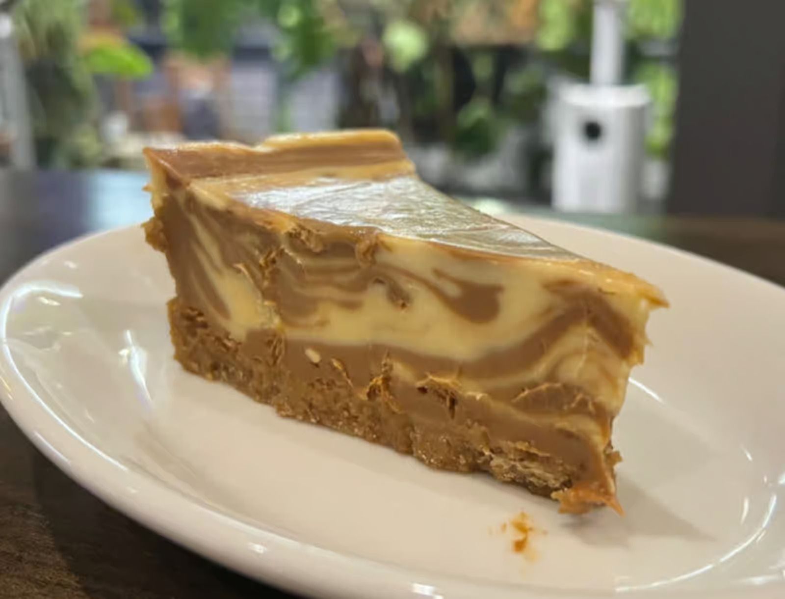 A slice of cheesecake is on a white plate on a table.