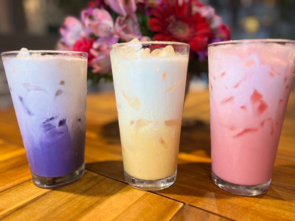 Three different colored milkshakes are sitting on a wooden table.