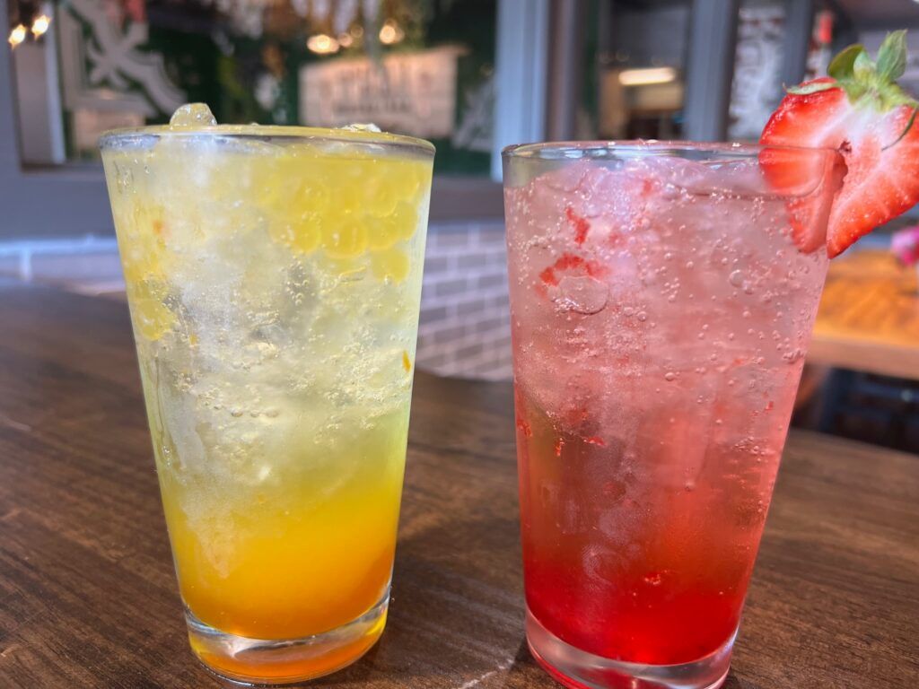 Two drinks , one orange and one red , are on a table.