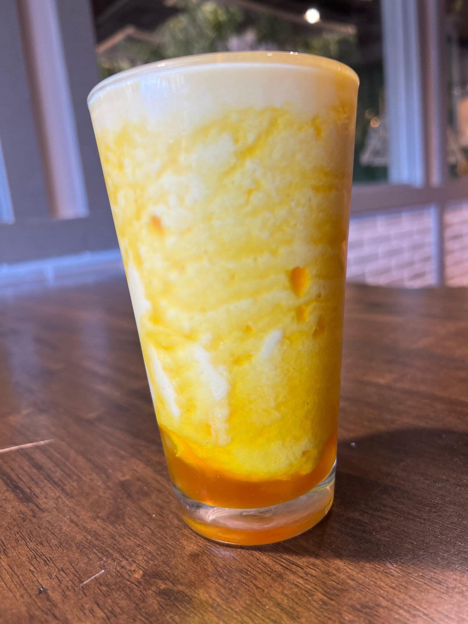 A glass of yellow liquid is sitting on a wooden table.