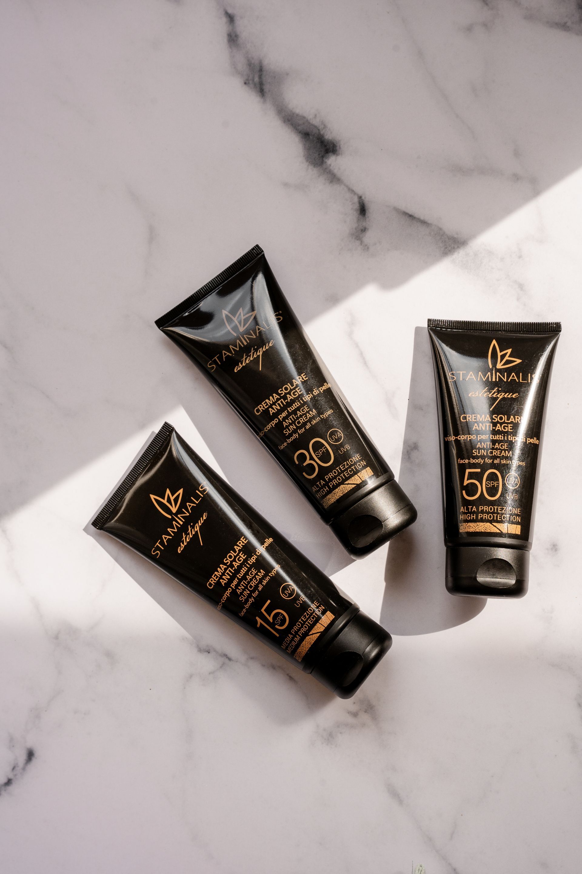 Tre tubetti di crema solare sono appoggiati su una superficie di marmo.