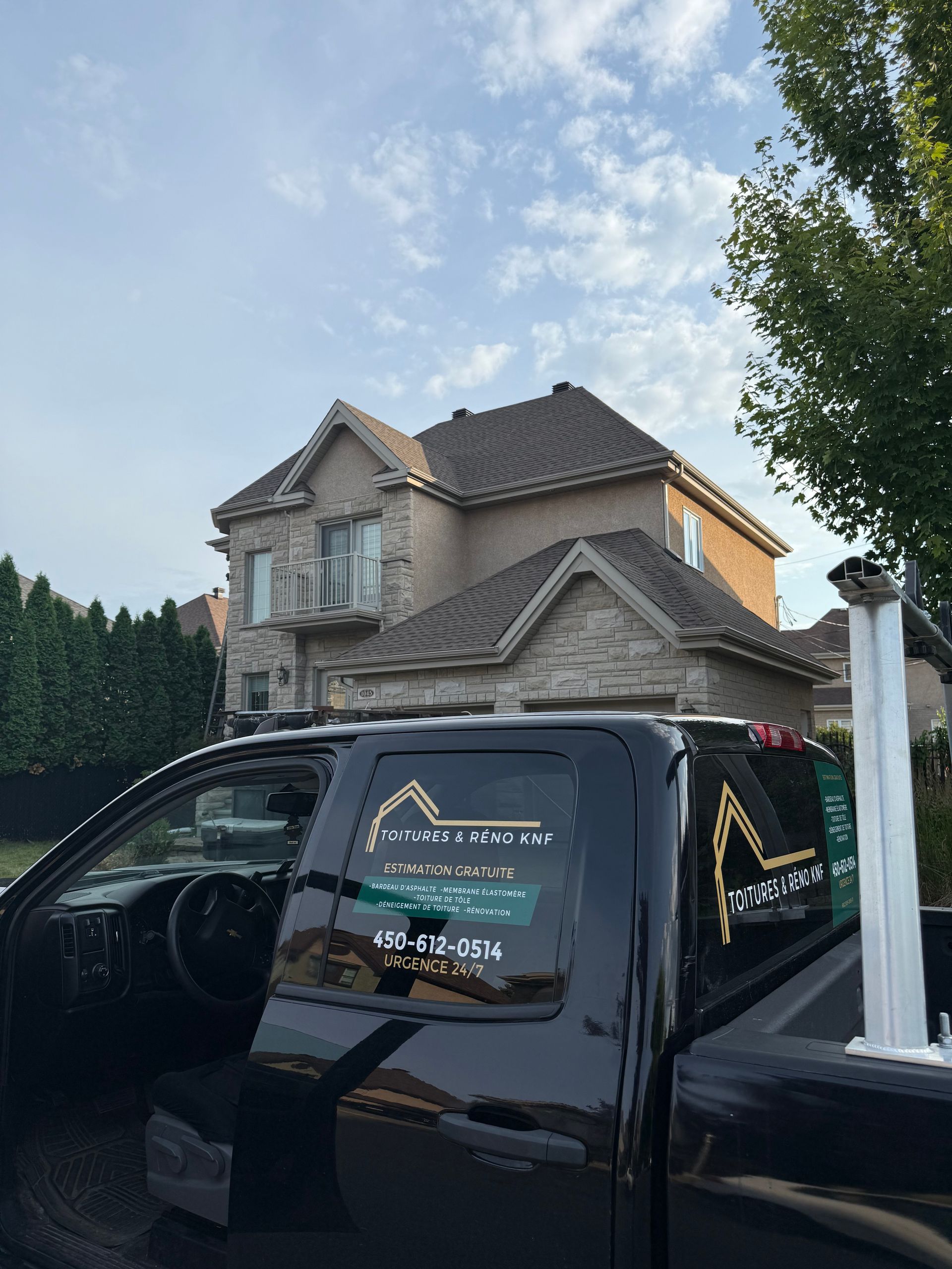 Camion noir garé devant une maison en briques beiges sous un ciel bleu.