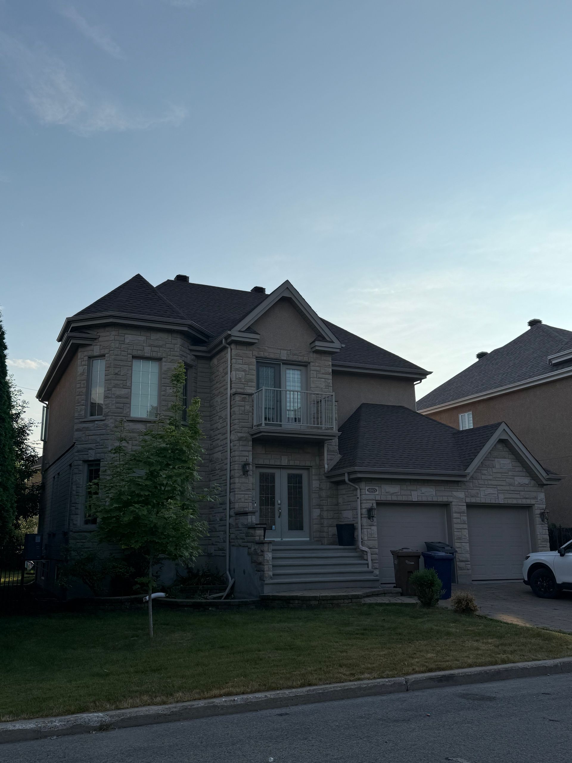 Maison en pierre avec garage double. Entrée avec balcon. Ciel bleu en arrière-plan.