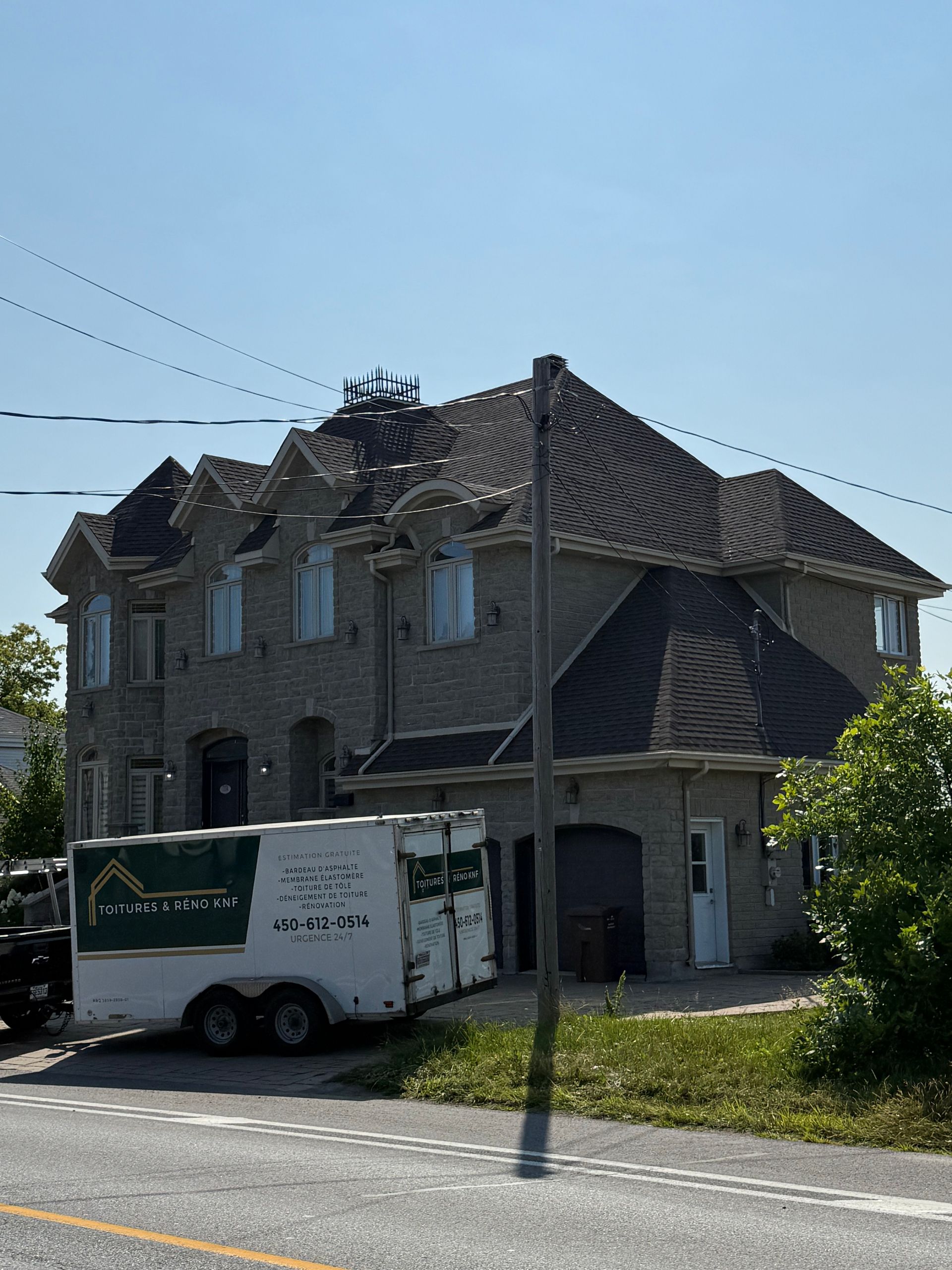 Maison en briques à deux étages avec toit sombre. Une caravane blanche garée devant. Ciel bleu.