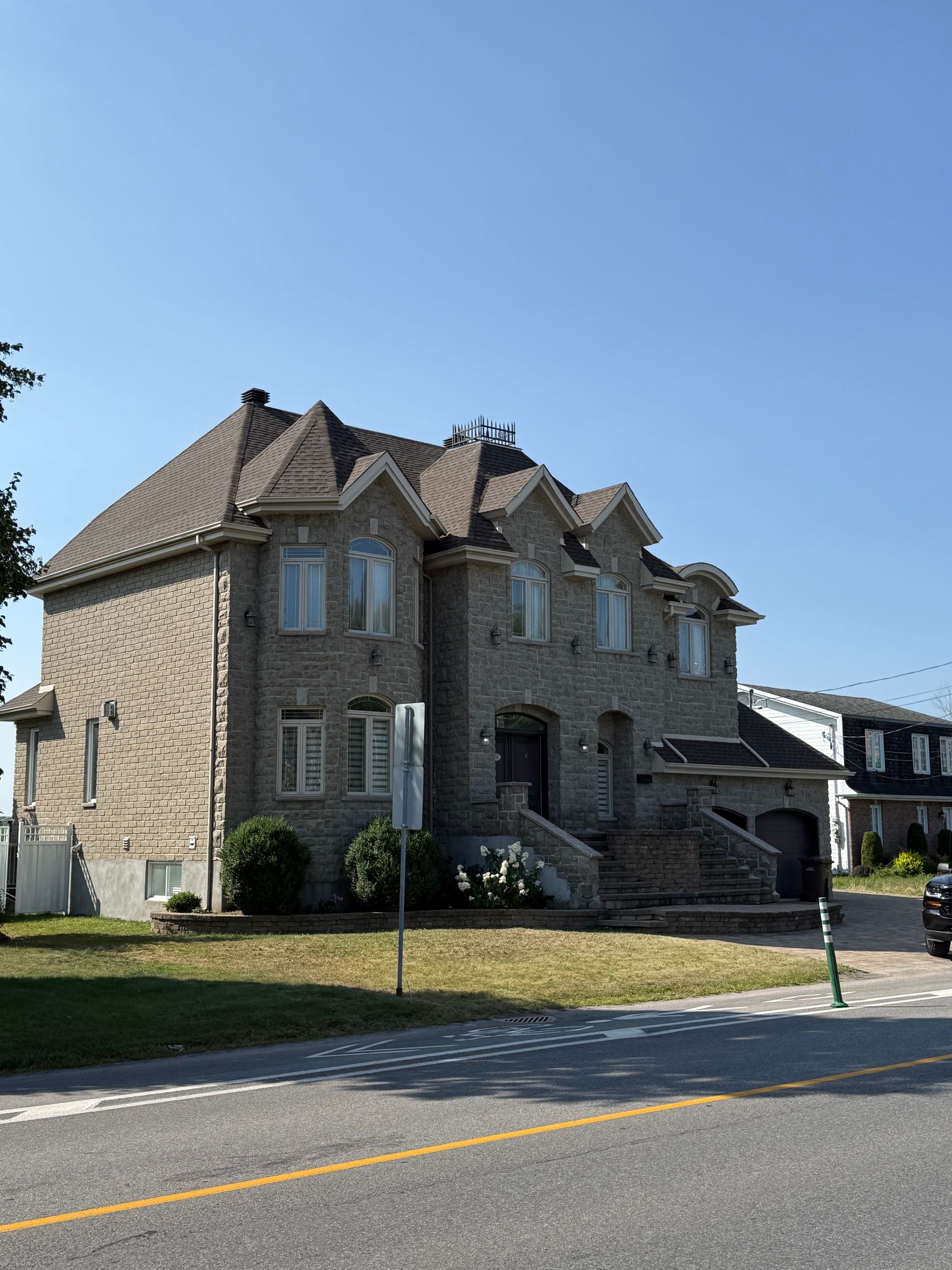Maison en pierre à deux étages avec des toits en pointe décoratifs, des fenêtres et une petite pelouse par une journée ensoleillée.