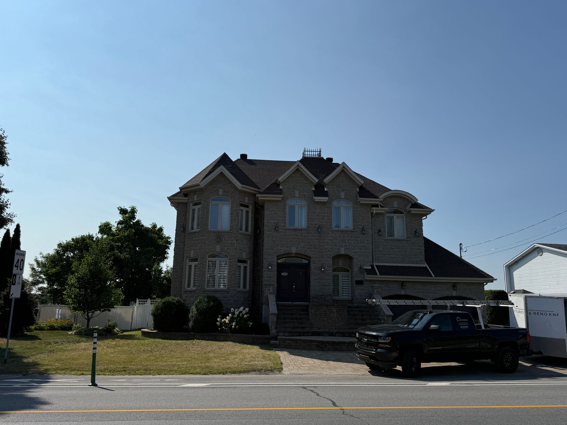 Maison à façade en pierre avec camion noir garé devant par une journée ensoleillée.