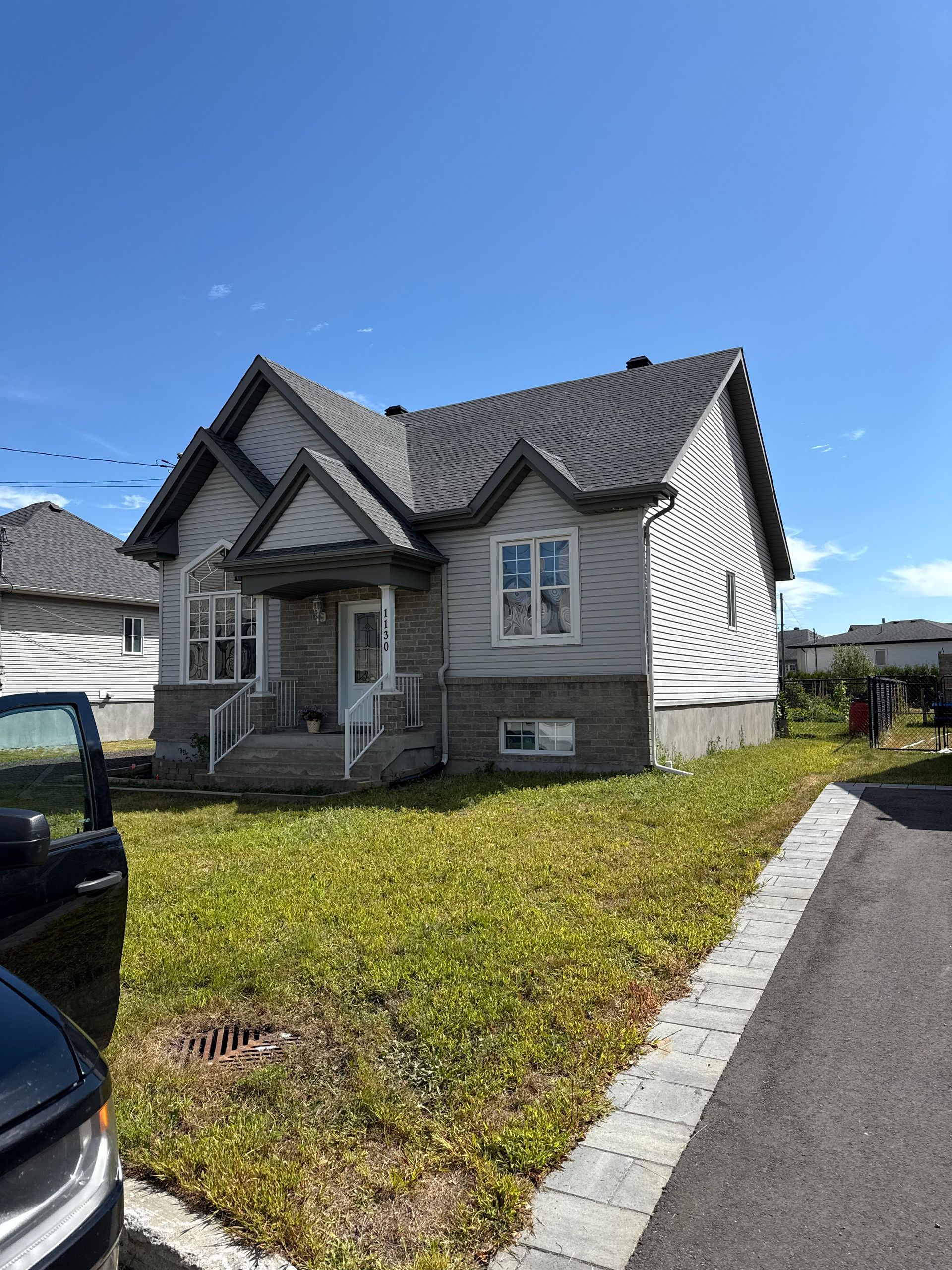 Maison grise avec pelouse verte, trottoir et ciel bleu.