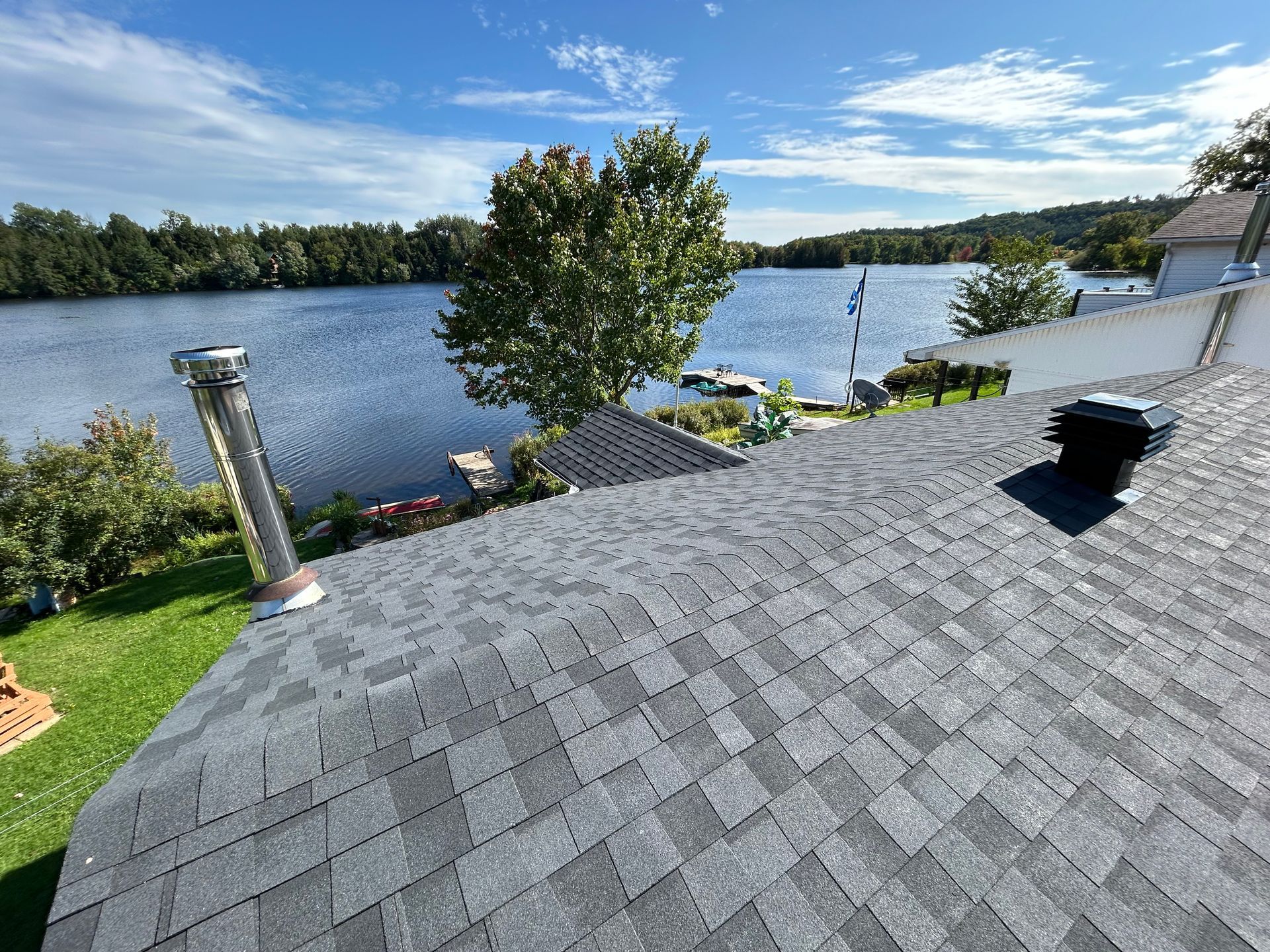 Toit en bardeaux gris donnant sur un lac avec des arbres et un ciel bleu.