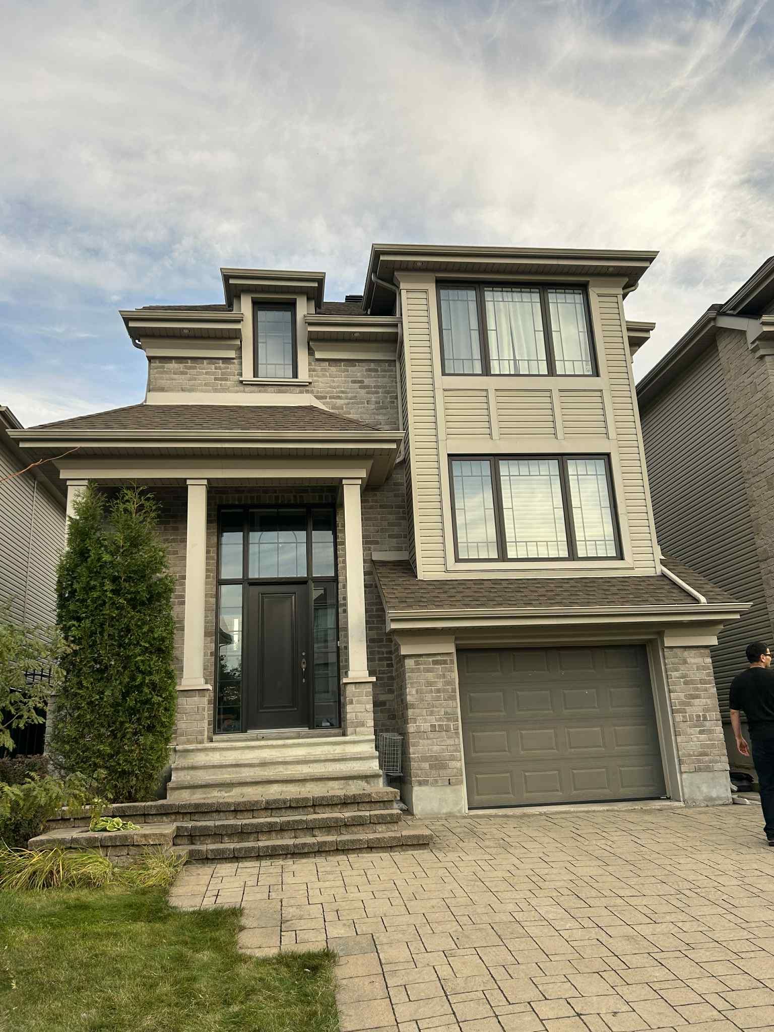 Maison à deux étages avec façade en pierre et touches de brun clair. Comprend un perron, un garage et une porte d'entrée.