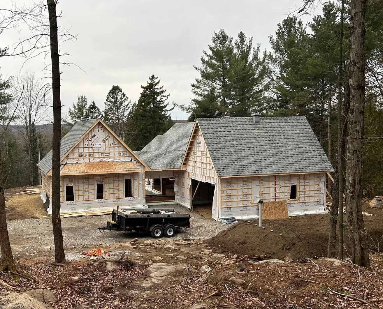 Construction d'une maison avec une caravane garée devant. Le toit est recouvert de bardeaux. Des arbres entourent le bâtiment.