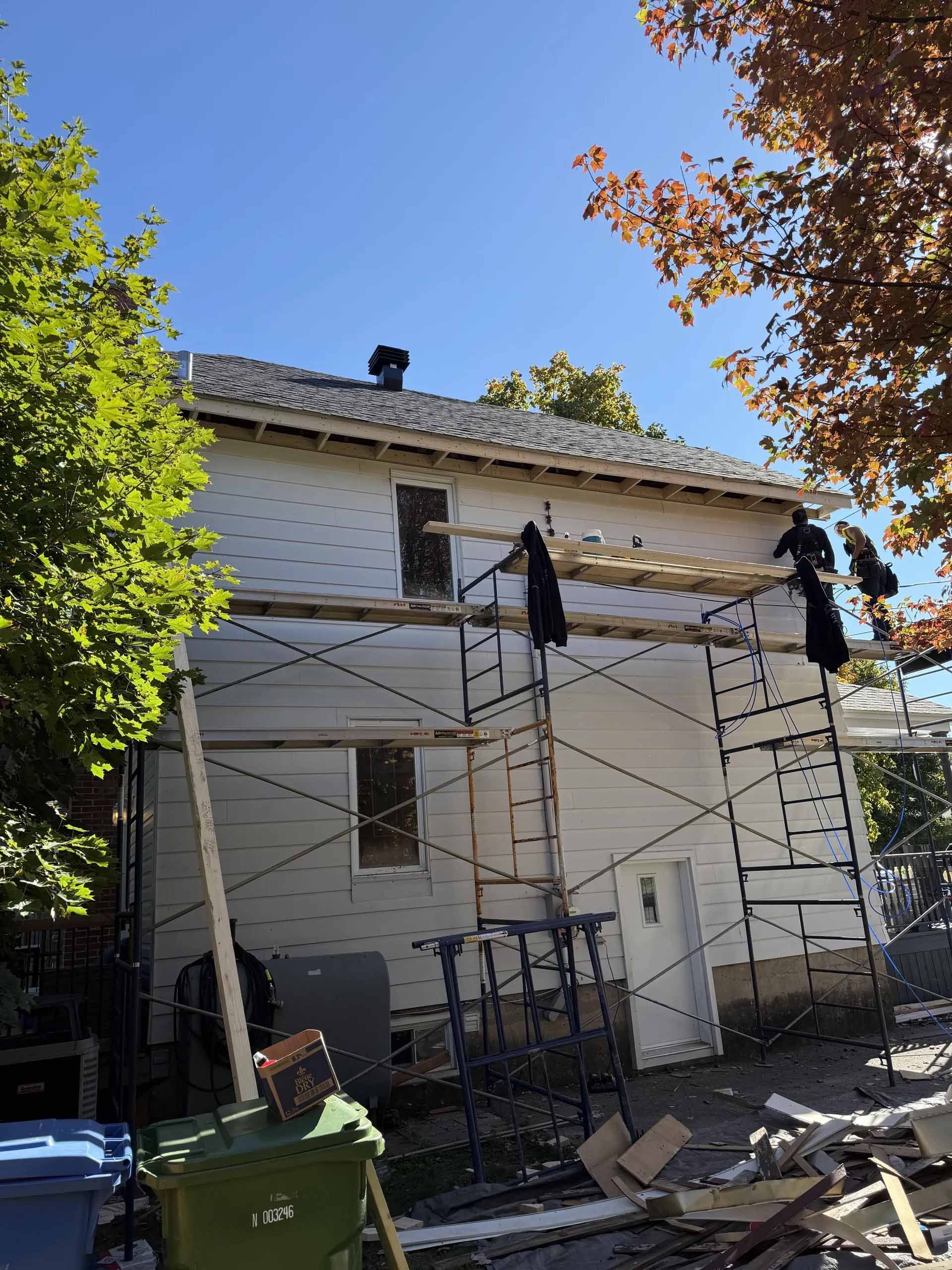 Extérieur d'une maison en rénovation ; échafaudage avec ouvriers. Revêtement blanc, ciel bleu.
