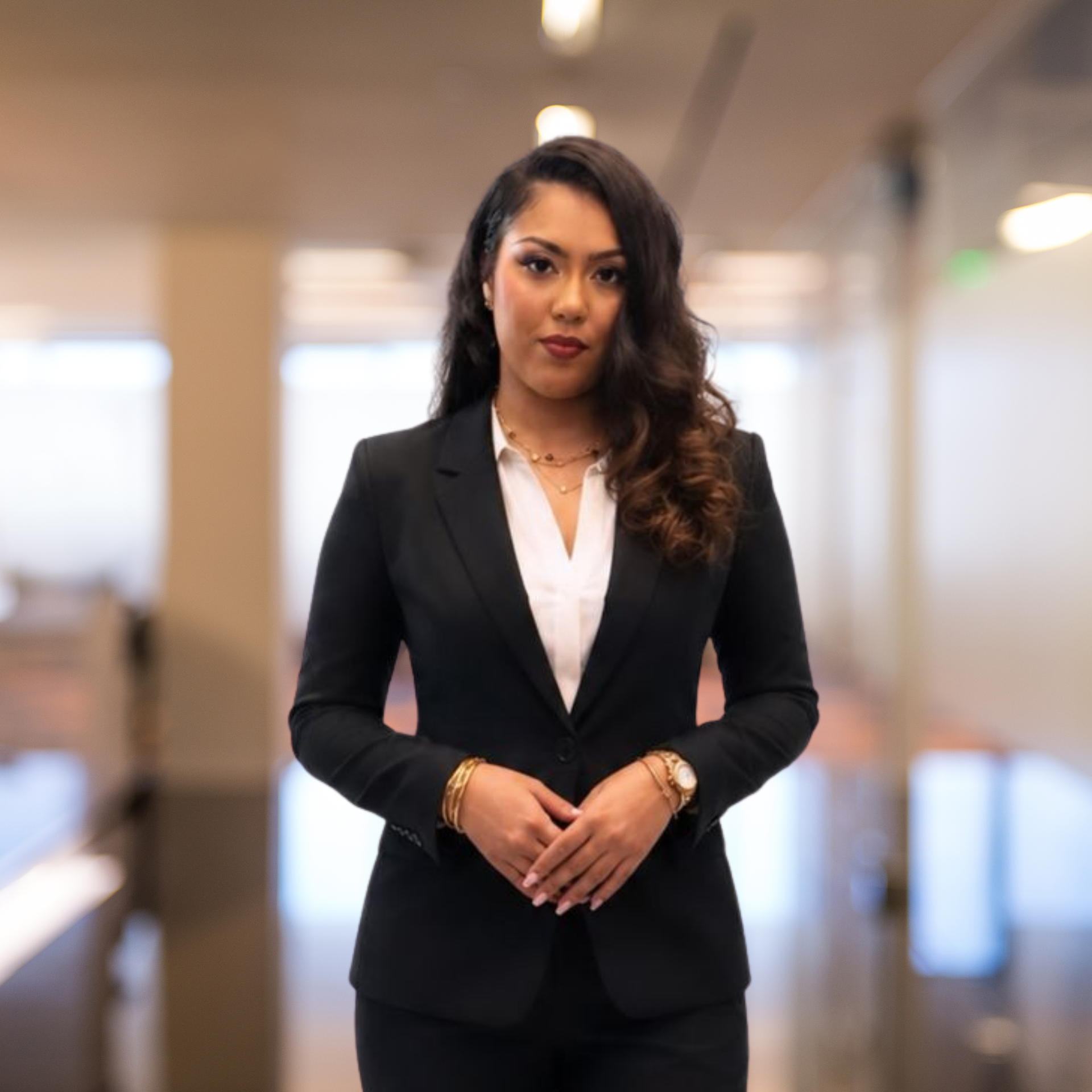 Woman in a black suit standing in an airport lounge with planes visible through large windows