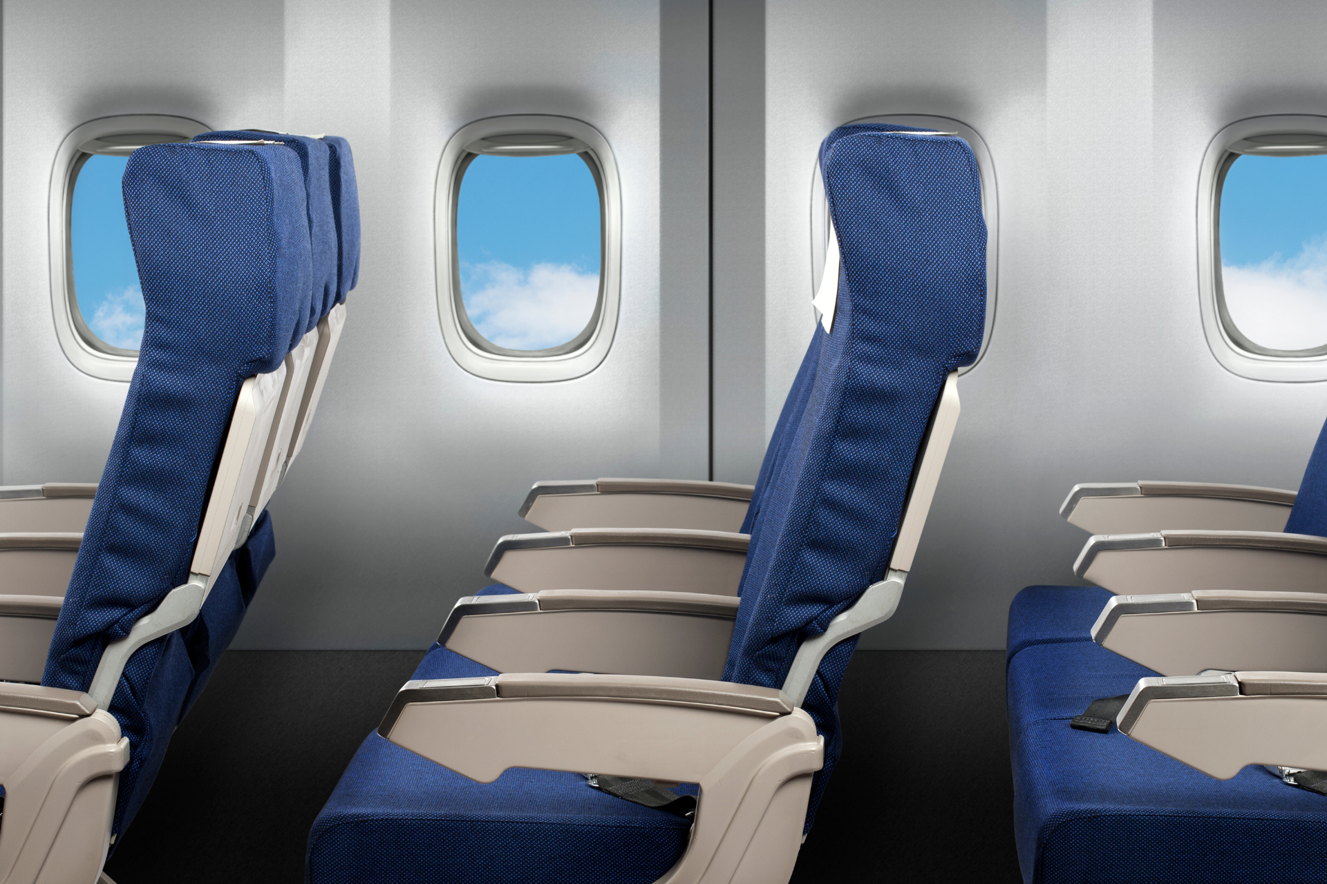 Airplane cabin seats with blue upholstery and tray tables by oval windows
