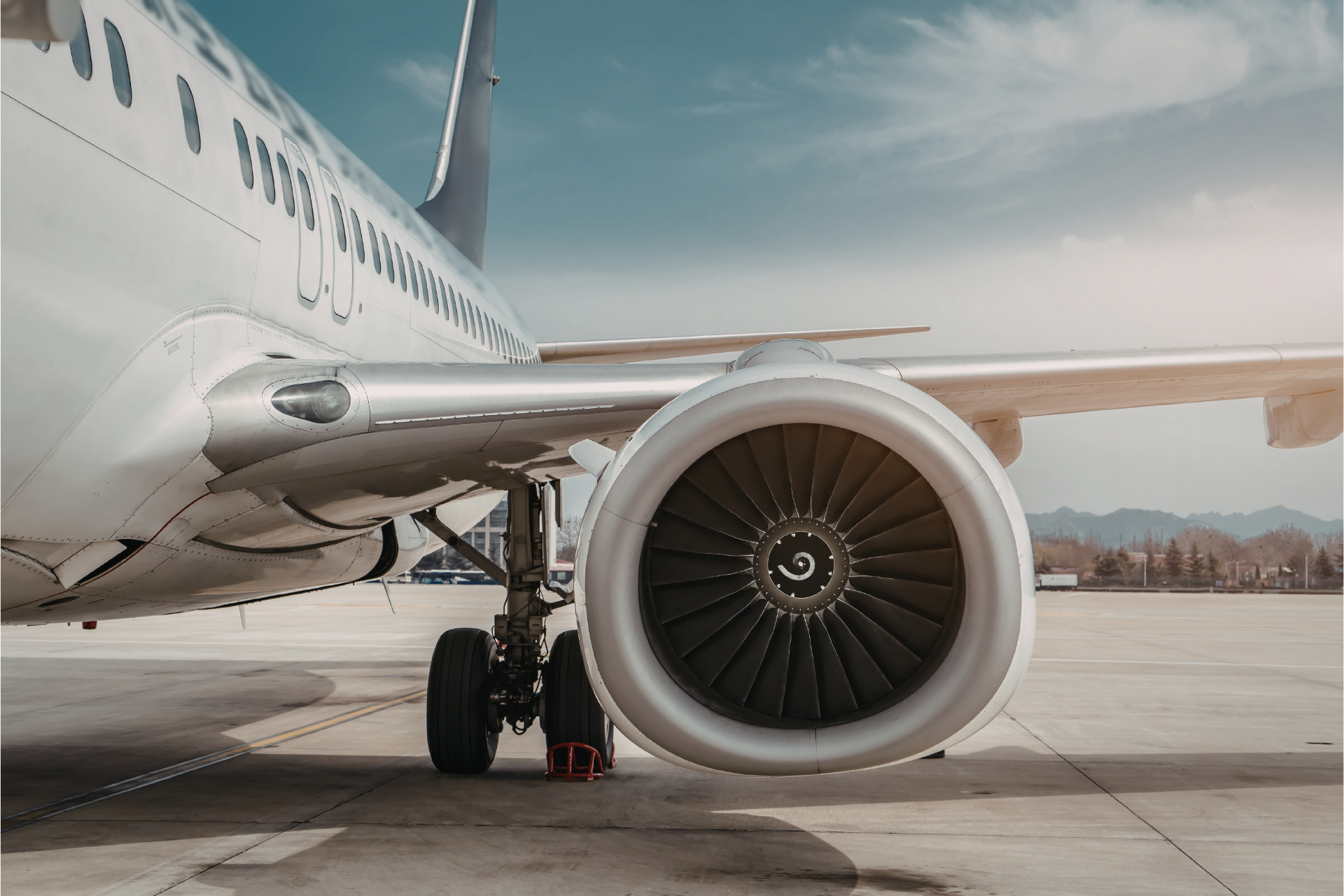 Close-up of a white airplane engine and wing on a runway with mountains in the background