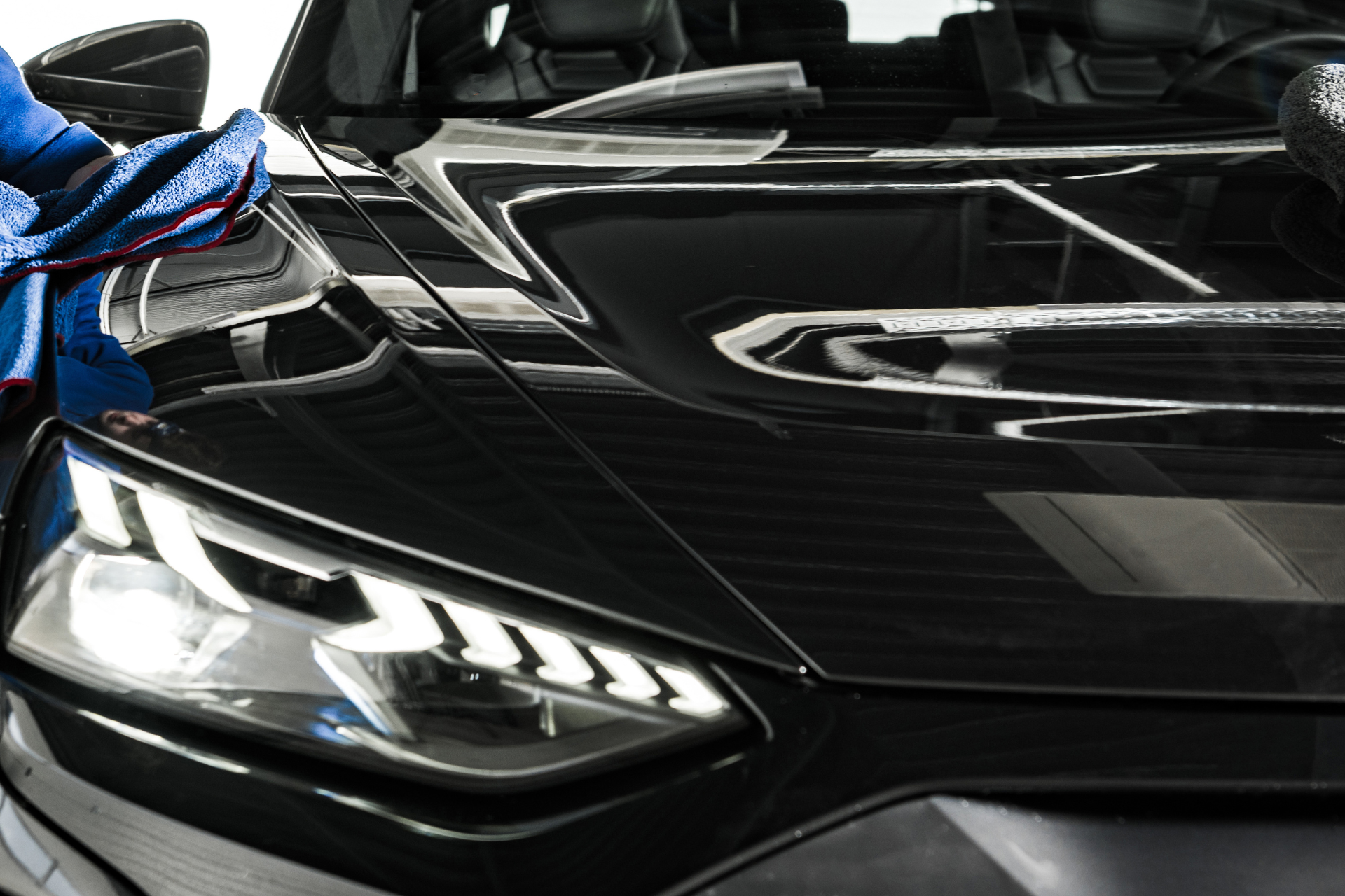 Close-up of a black sports car hood and headlight with a blue cloth on the fender