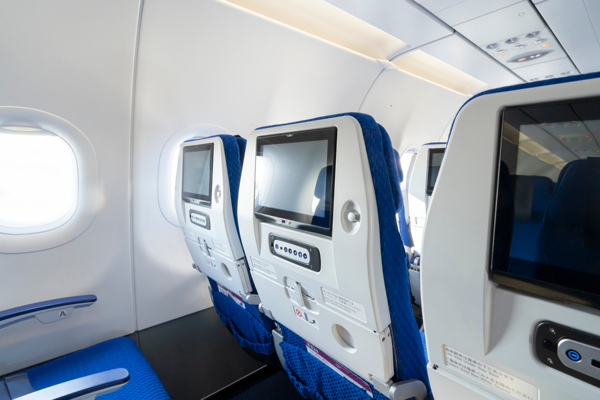 Airplane cabin with blue seats and personal entertainment screens by the windows