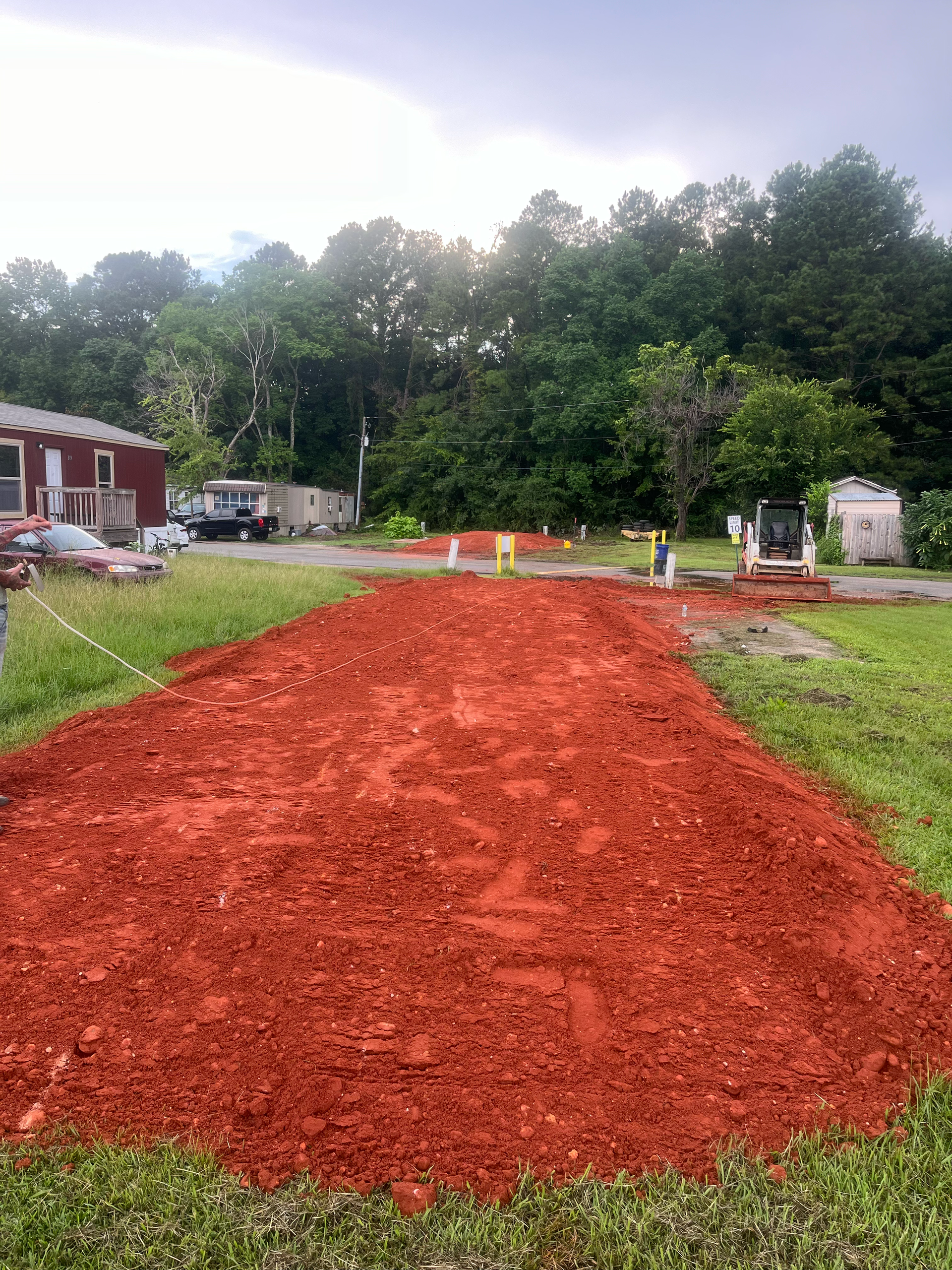 A pile of red mulch spread across a grassy yard, with a building and heavy equipment visible in the background.