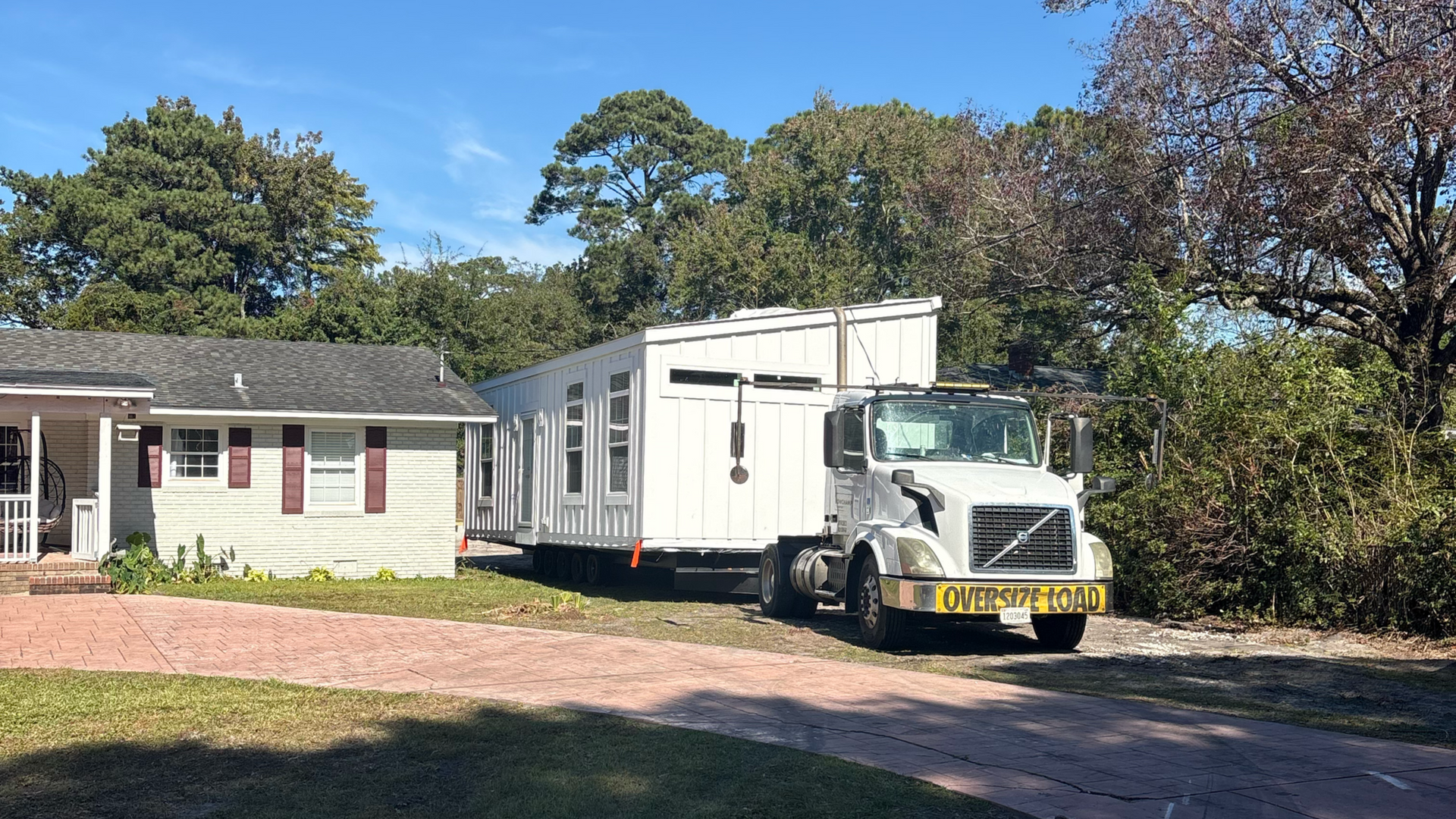 White moving truck parked beside a small house on a sunny day with trees in the background