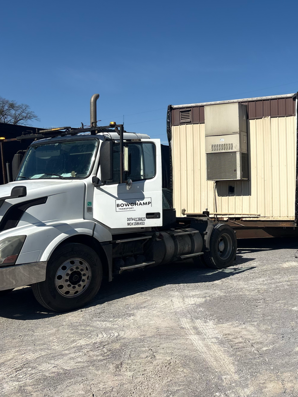 A white semi-truck parked outdoors, towing a tan storage trailer with a mounted HVAC unit.