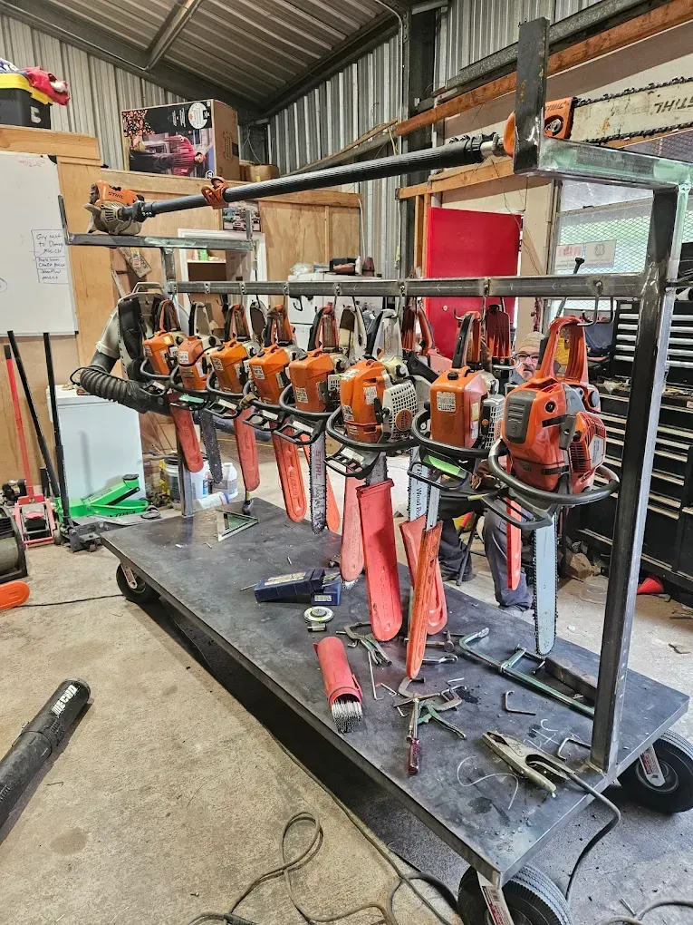 A cart holding numerous orange chainsaws with safety guards, in a cluttered workshop setting.