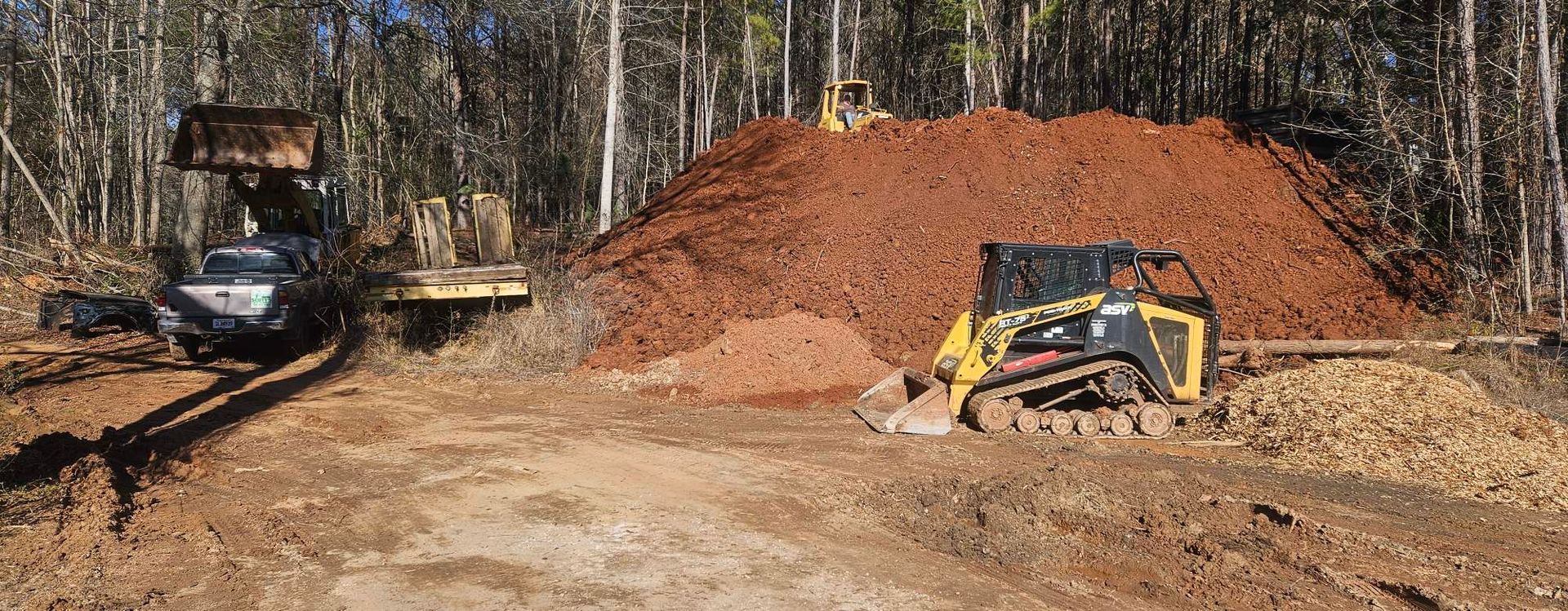 Construction site with heavy machinery, including a skid steer and excavator, moving earth.