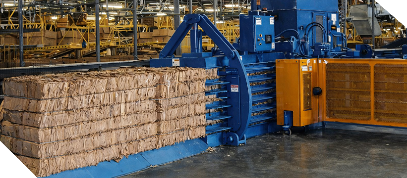 A large industrial cardboard baling machine in a facility, compressing recycled paper into a compact, rectangular bale.