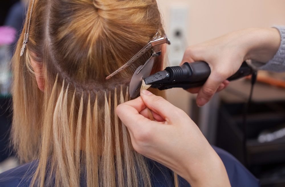 A Woman Is Getting Her Hair Extensions Done By A Hairdresser — Elements Hair Artists In Belmont, NSW