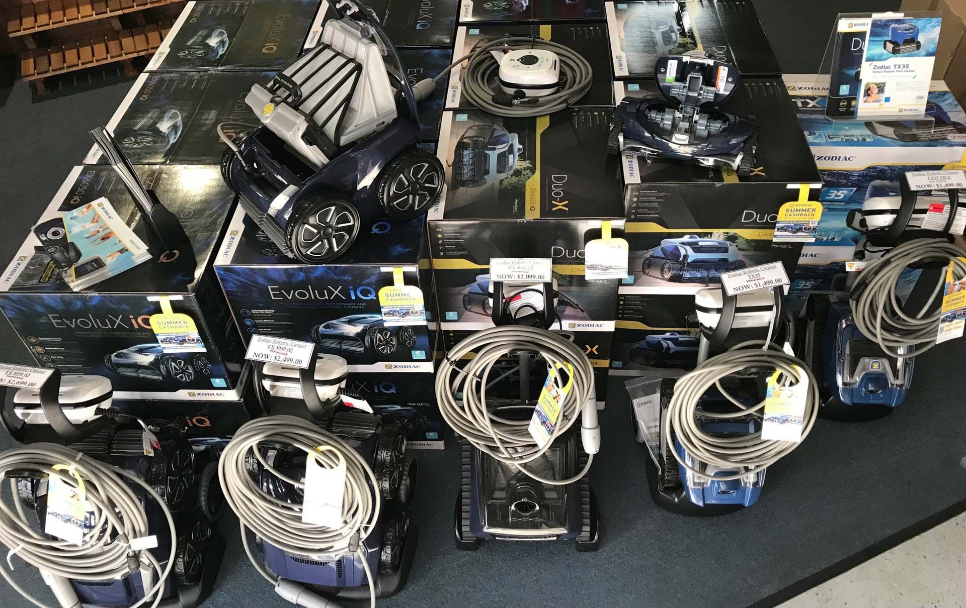 A Collection Of Black Electronics With Cables, Some In Boxes, On A Wooden Surface