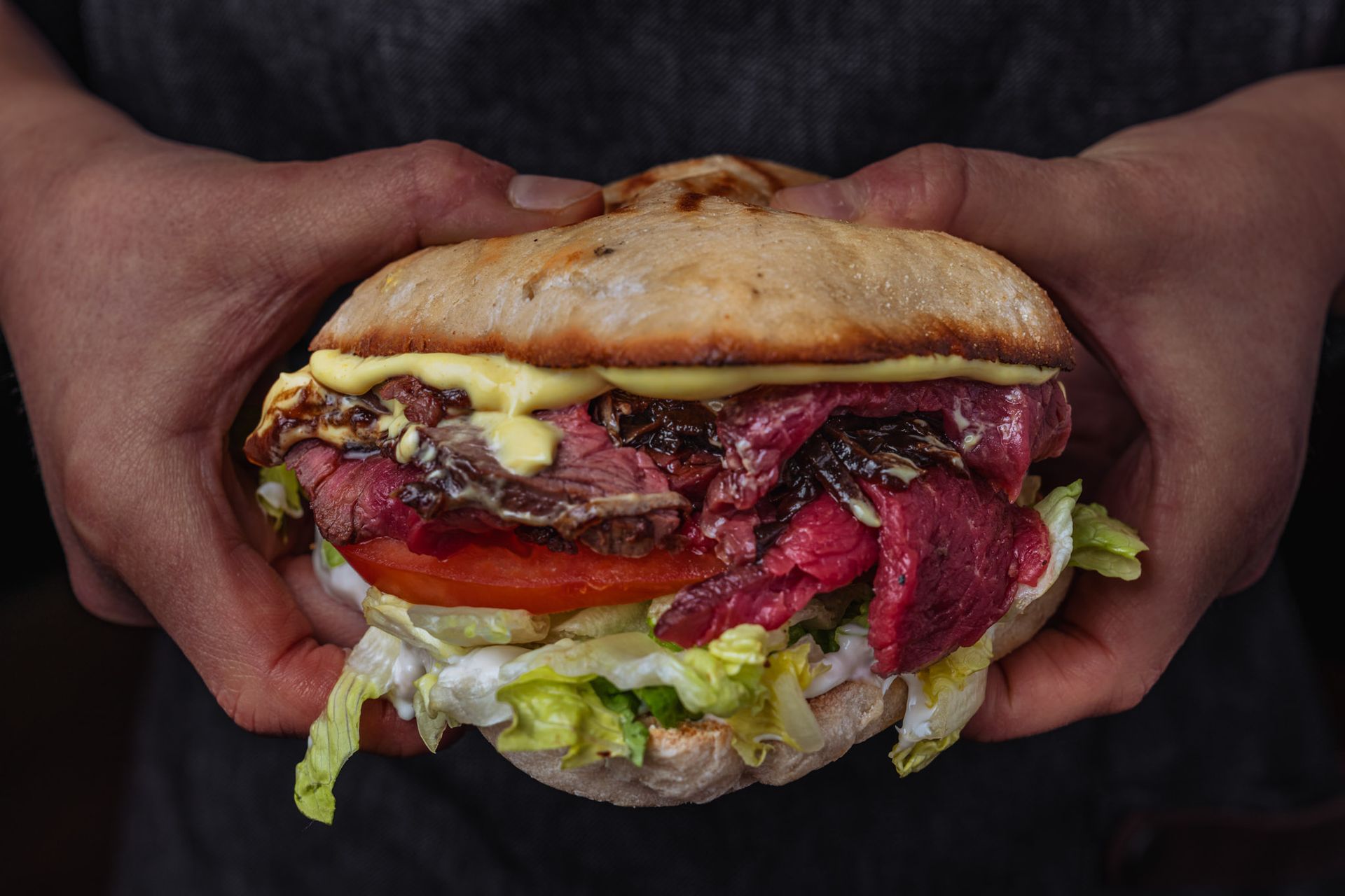 Steak dinner: someone pours sauce onto a ribeye, alongside fries and salad. Other person's steak and wine visible.