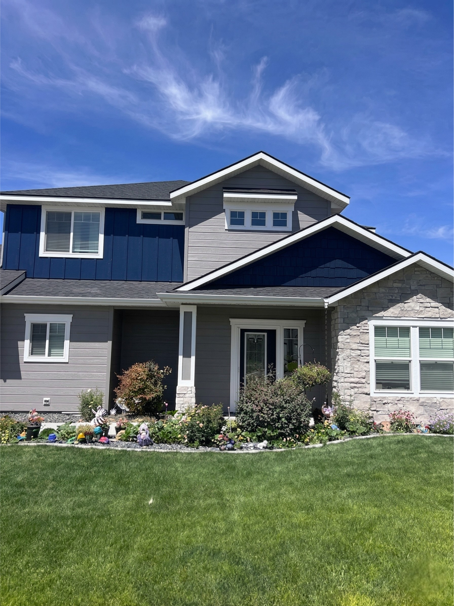 Beige and brown house with gray roof, small front yard, cloudy sky.