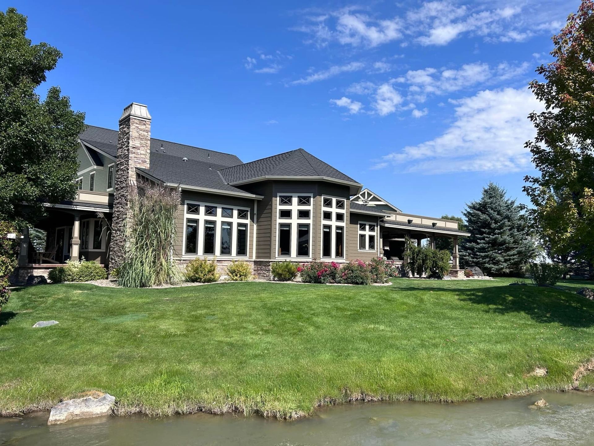 Large, multi-story house with green lawn, pond, and blue sky.